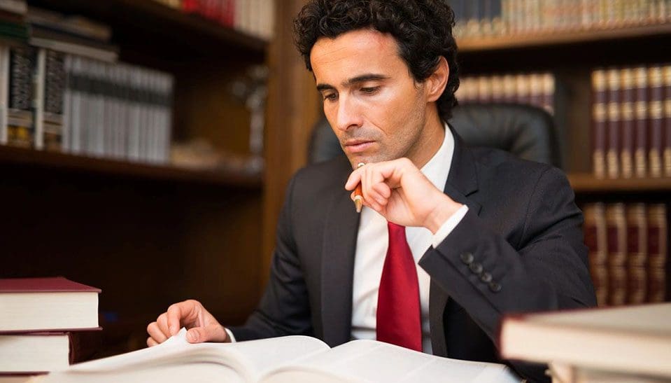 A man in suit and tie sitting at table with book.