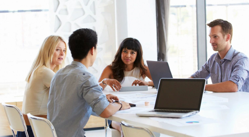 A group of people sitting at a table with laptops.